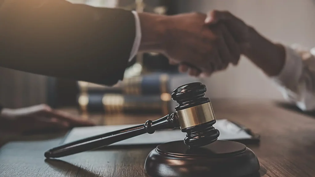 Gavel on a desk with two people shaking hands in the background.